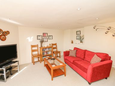 A living room with a red sofa wooden coffee table wooden chairs and television at West Henstill House in Sandford Devon