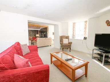A living room with a red sofa a wooden coffee table an armchair and a television at West Henstill House in Sandford Devon