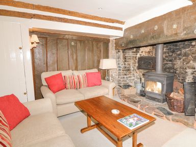 A living room with beige sofas red cushions a wooden coffee table and a wood burning stove at West Henstill House in Sandford Devon