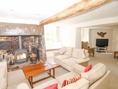 A living room with sofas a wooden coffee table a wood burning stove and a television at West Henstill House in Sandford Devon