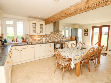 A kitchen with white cabinets wooden chairs around a table and windows at West Henstill House Sandford Devon