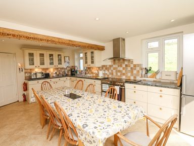 A kitchen with a dining table covered by a tablecloth and wooden chairs at West Henstill House in Sandford Devon