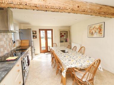 A kitchen with a dining table covered with a tablecloth and wooden chairs at West Henstill House in Sandford Devon