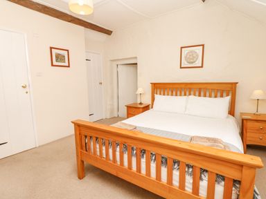 A bedroom with a wooden bed frame two bedside tables with lamps and framed pictures on walls at West Henstill House in Sandford Devon