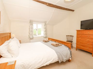 A bedroom with a wooden bed a window wooden dresser a wooden chair and a television at West Henstill House in Sandford Devon