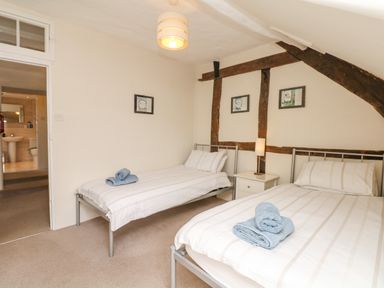 A bedroom with two single beds with blue towels on them a nightstand with a lamp and exposed wooden beams on the wall at West Henstill House in Sandford Devon