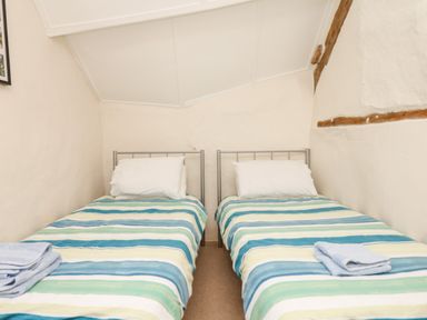 A bedroom with two single beds with striped bedding and folded towels at West Henstill House in Sandford Devon