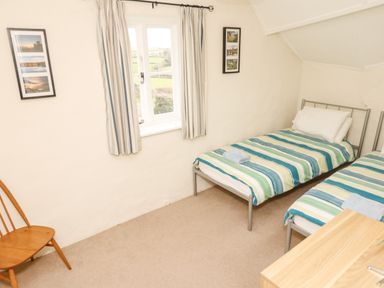 A small bedroom with two single beds striped bedding a wooden chair and framed pictures on the walls at West Henstill House in Sandford Devon