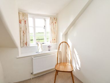 A wooden chair by a window with floral curtains and a radiator below at West Henstill House in Sandford Devon