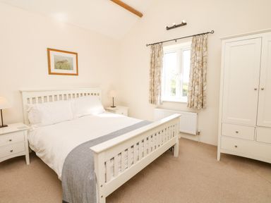 A bedroom with a white bed frame two bedside tables lamps a window with curtains and a white wardrobe at West Henstill House Sandford Devon