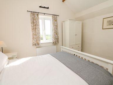 A bedroom with a bed a white wardrobe a window with curtains and a small bedside table at West Henstill House Sandford Devon