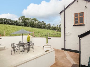 An outdoor patio with a round table and chairs under a large umbrella at West Henstill House in Sandford Devon