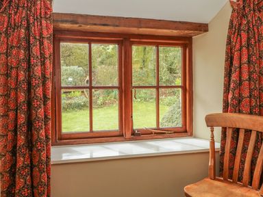 A window with wooden frame red patterned curtains and a wooden chair near the window at Hope Cottage in Riddlecombe near Winkleigh