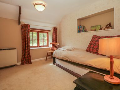 A bedroom with a single bed a wooden chair a window with patterned curtains and a bedside table with a lamp at Hope Cottage in Riddlecombe near Winkleigh