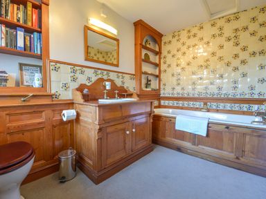 A bathroom with wooden vanity and bathtub with tiled walls and shelves with books at Hope Cottage in Riddlecombe near Winkleigh