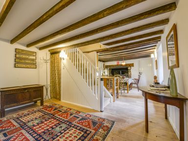 A rustic hallway with wooden beams a stairway a patterned rug and a dining area at Hope Cottage in Riddlecombe near Winkleigh