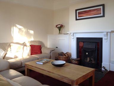 A living room with beige sofas a wooden coffee table a fireplace and a basket of firewood at Hedgelea in North Tawton