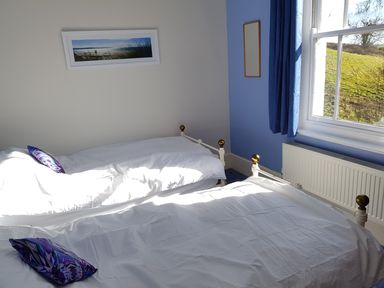 A bedroom with two single beds with white bedding and blue pillows next to a window with blue curtains at Hedgelea in North Tawton