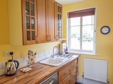 A kitchen with wooden cabinets a double sink a dish rack a kettle and a window with blinds at Hedgelea in North Tawton