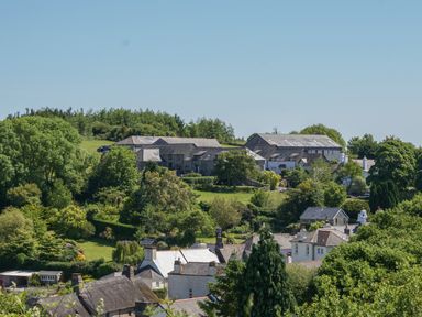 Green hillside with houses and trees under blue sky at Linney Cottage in Dittisham