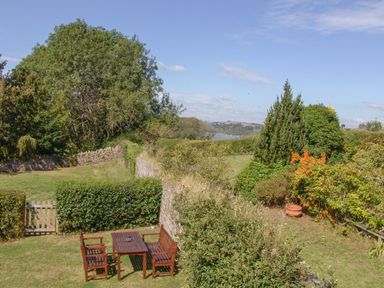 A garden with wooden table and chairs surrounded by hedges and trees at Linney Cottage in Dittisham