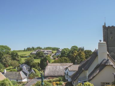 Houses with thatched roofs and a stone church tower in a village with trees and fields at Linney Cottage in Dittisham