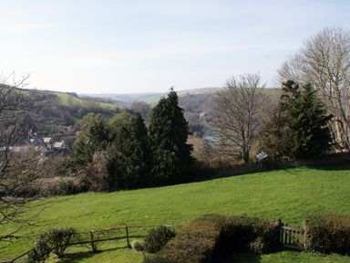A grassy field with trees and hedges overlooking hills and a river at Linney Cottage in Dittisham