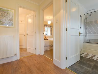 A hallway with three open doors showing a bedroom a bathroom and another room at Linney Cottage in Dittisham