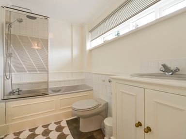 A bathroom with a bathtub shower combination toilet sink and cabinet at Linney Cottage in Dittisham