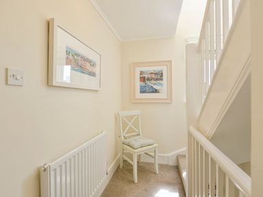 A staircase landing with a white chair with a cushion and two framed pictures on the wall at Linney Cottage in Dittisham