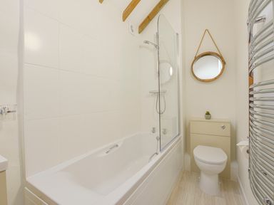 A bathroom with a bathtub shower combination a round mirror and a toilet at Bramble Cottage in Ringmore