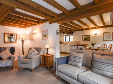 A living room with armchairs and a sofa next to a kitchen and dining area at Bramble Cottage in Ringmore