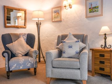 A sitting area with two armchairs a wooden side table with a lamp a floor lamp and framed artwork on the walls at Bramble Cottage in Ringmore