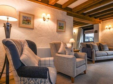 A living room with armchairs a sofa lamps framed pictures and wooden ceiling beams at Bramble Cottage in Ringmore