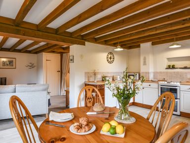 A kitchen and dining area with wooden table chairs flowers bread and fruit at Bramble Cottage in Ringmore