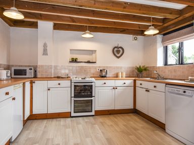 A kitchen with wooden beams white cabinets appliances and a window at Bramble Cottage in Ringmore