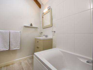 A bathroom with a bathtub a sink with a mirror above and two white towels hanging on a rail at Bramble Cottage in Ringmore