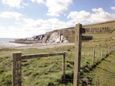 A coastal path signpost beside a fence with cliffs and beach in the background at Bramble Cottage in Ringmore