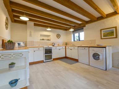 A kitchen with white cabinets wooden beams on the ceiling and appliances at Bramble Cottage Ringmore