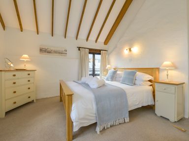 A bedroom with a wooden bed frame, two bedside tables with lamps, a chest of drawers, and exposed wooden ceiling beams at Bramble Cottage in Ringmore