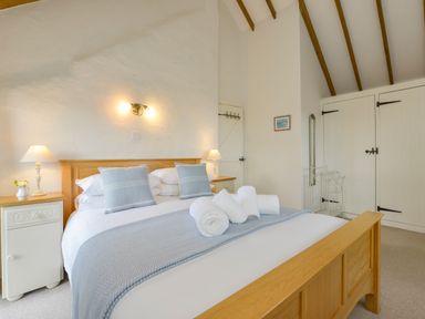 A bedroom with a wooden bed with folded towels pillows and nightstands with lamps at Bramble Cottage in Ringmore