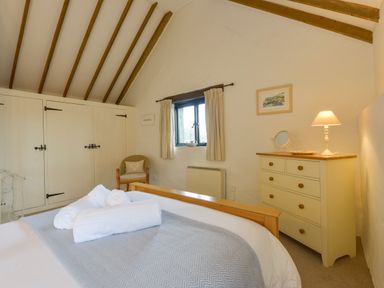 A bedroom with a bed with towels a chest of drawers with a lamp a chair and built in cupboards at Bramble Cottage in Ringmore