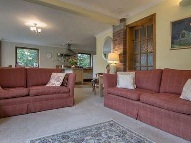 A living room with two red sofas and a lamp next to a wooden door at Galanda Treetops in Newton Ferrers