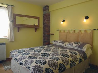 A bedroom with a bed with patterned bedspread and pillows next to a window with curtains and a wall mirror at Galanda Treetops in Newton Ferrers