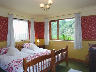 A bedroom with two single beds and windows showing greenery at Galanda Treetops in Newton Ferrers