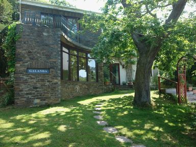 A stone house with large windows and a tree in front at Galanda Treetops in Newton Ferrers