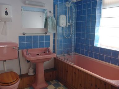 A bathroom with pink toilet sink and bathtub blue tiled walls shower and a window at Galanda Treetops in Newton Ferrers