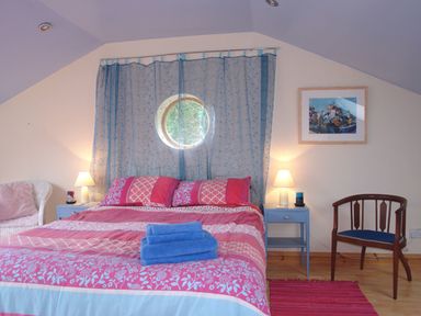A bedroom with a double bed with red and pink bedding and blue towels on top at Galanda Treetops in Newton Ferrers