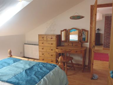 A bedroom with a wooden bed a chest of drawers a vanity table with mirror and a chair at Galanda Treetops in Newton Ferrers