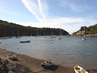 A river with boats moored and small boats on a pebble shore at Galanda Treetops in Newton Ferrers